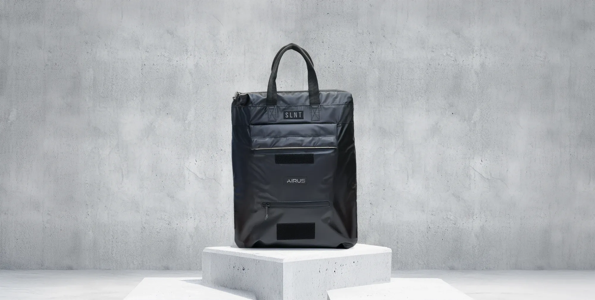 The AIRUS carry bag on a concrete plinth against a concrete wall.
