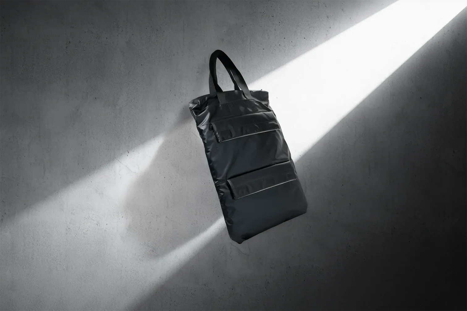 The AIRUS carry bag against a concrete wall, crossed by a shaft of daylight.