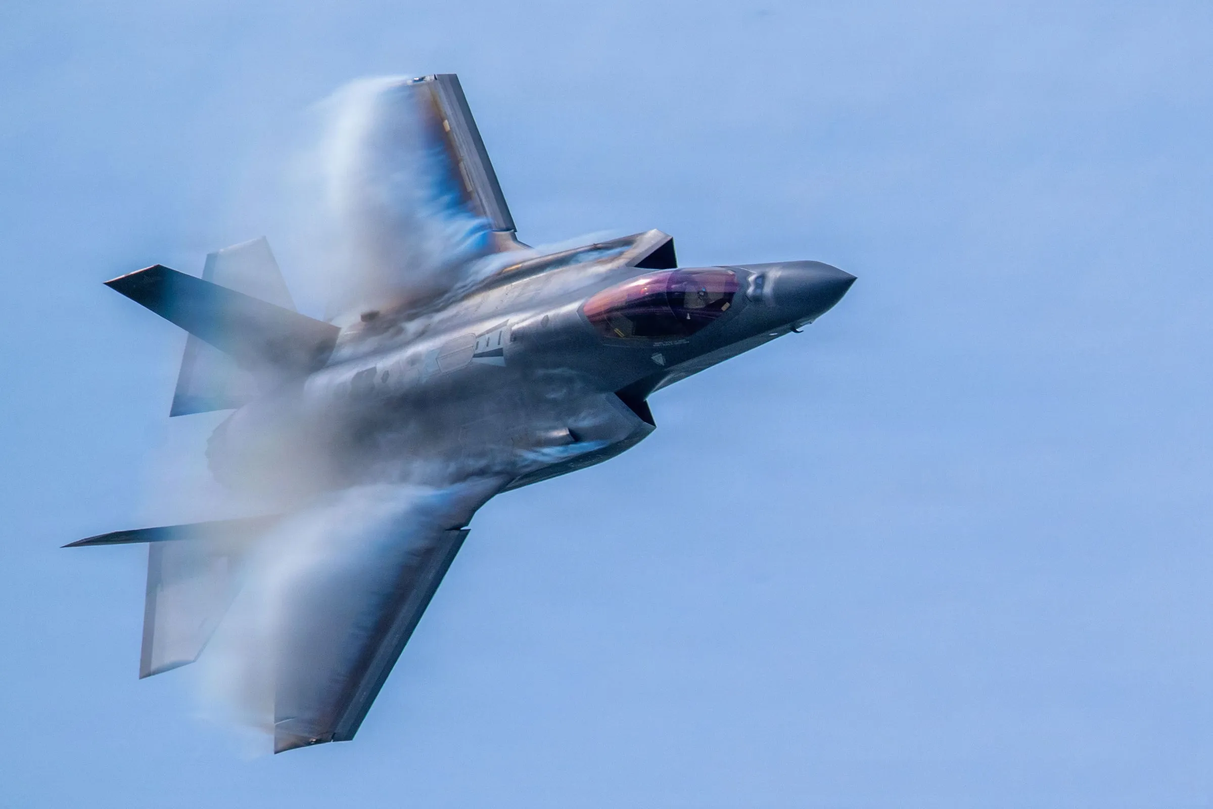 An F-35 banking hard, vapour forming over the wings.