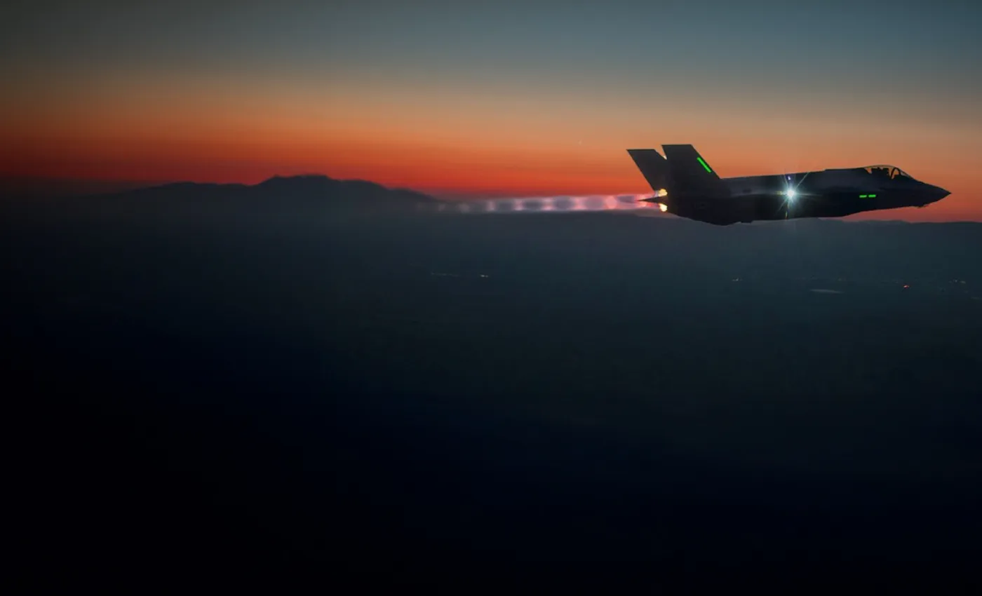 An F-35 in afterburner against a dusk horizon.